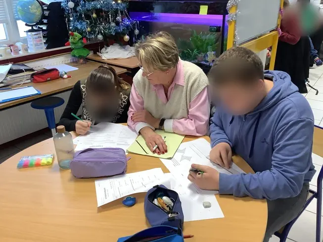 Une AESH accompagne deux élèves qui travaillent autour d’une table.