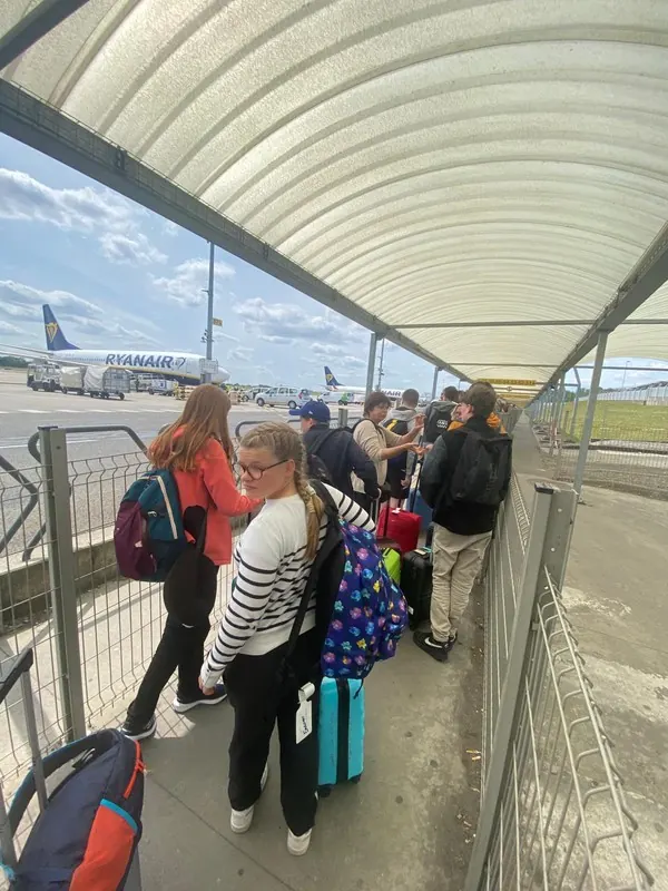 Des élèves et leurs accompagnateurs, de dos, dans un aéroport au départ du voyage Erasmus+ en Italie.