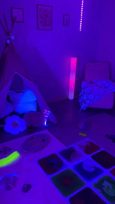 La salle Snoezelen du collège, plongée dans une lumière violette, avec des tapis sensoriels au sol.